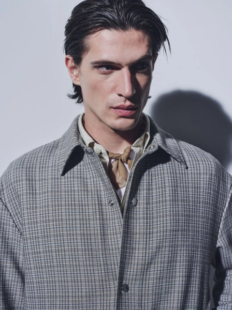 Portrait of a young adult male with dark hair, wearing a plaid overshirt and a scarf, posing in a photo studio setting.