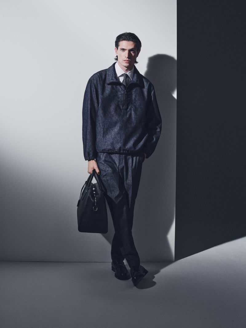 Model in dark jacket and trousers holding a black handbag against a studio backdrop for BOSS