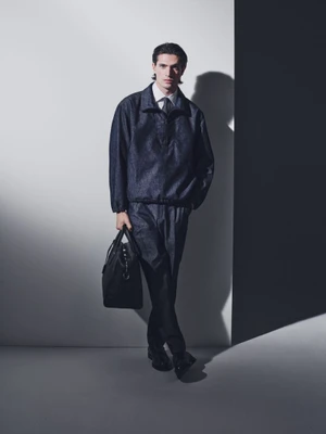 Model in dark jacket and trousers holding a black handbag against a studio backdrop for BOSS