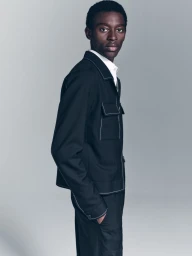 Model wearing dark jacket with white topstitching against a neutral grey studio background