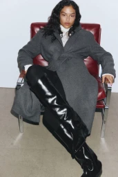 Model Devyn Garcia seated on a red leather armchair wearing a grey coat and black boots for H&M AW2025