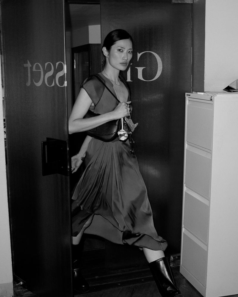 Elegant Asian woman in stylish dress and black boots entering through a doorway in a monochrome fashion shot, holding purse.