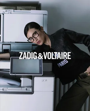 Model wearing black leather jacket and glasses leaning on a large office copy machine for Zadig and Voltaire