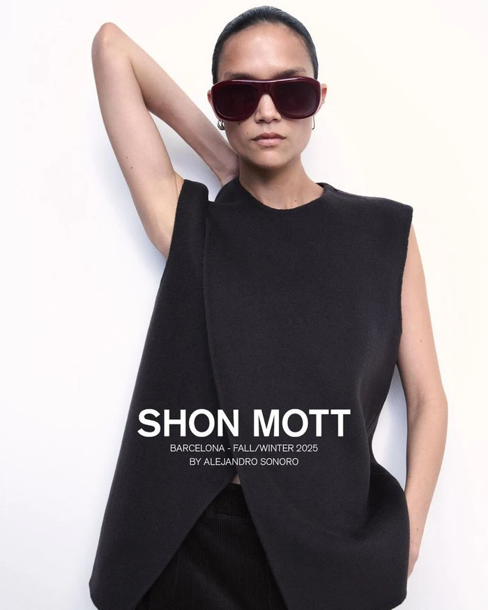 Model wearing oversized dark sunglasses and a structured black sleeveless top against a white studio background.