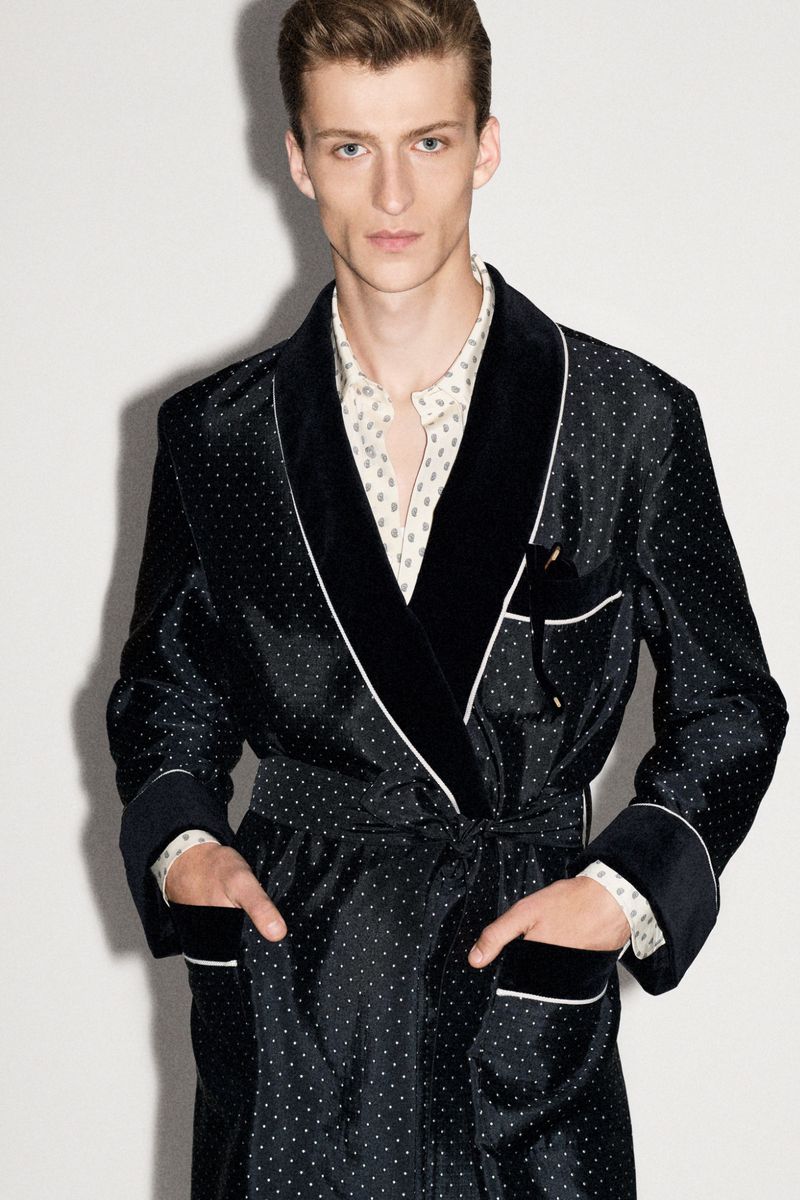Elegant adult male model in a black polka-dot silk robe with velvet lapels and hands in pockets, posing against a white background.