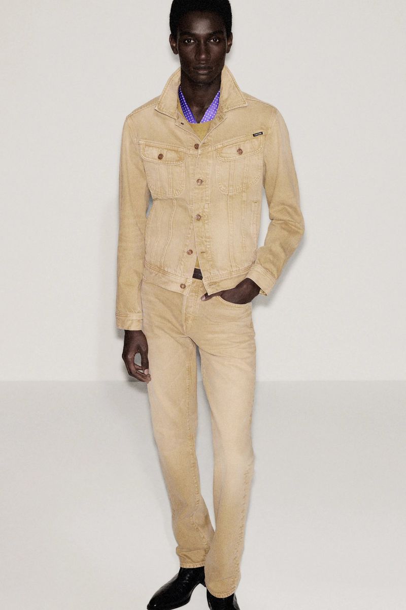 Full-length studio shot of a dark-skinned male model in a light tan denim jacket and matching jeans, hands in pockets, against white backdrop.