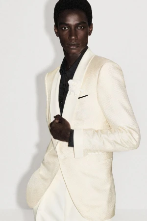 Model in an ivory shawl-lapel dinner jacket and black shirt against a plain white studio background.