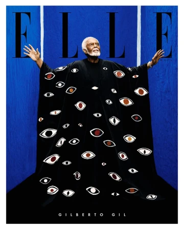 Magazine cover featuring an adult male with a beard wearing a black robe with eyes printed on it, against a blue background.