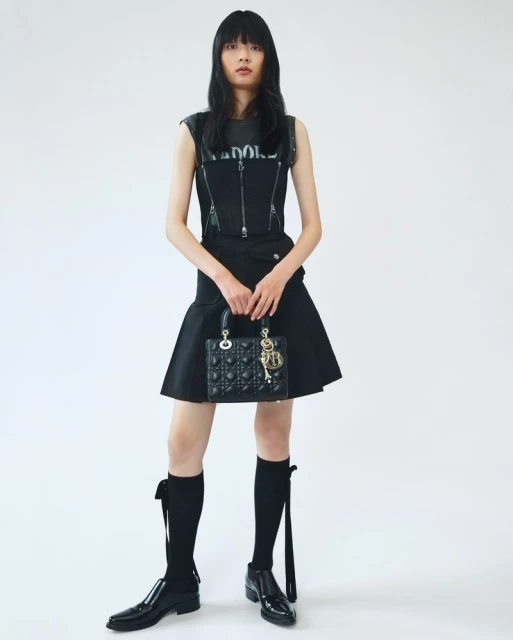 Asian woman in black outfit holding a purse against a white backdrop, fashion editorial shot, high contrast, studio lighting.