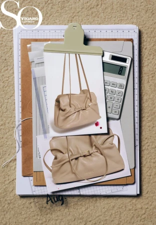 Fashion still life with a beige purse displayed on photograph attached to a clipboard, along with a calculator and papers.