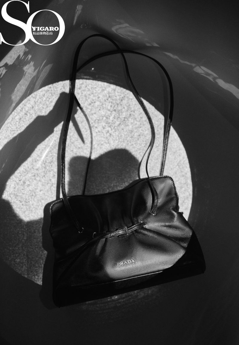 Black Prada handbag with handle straps and a light spotlighting the center of the bag, showcasing the brand logo on the front.