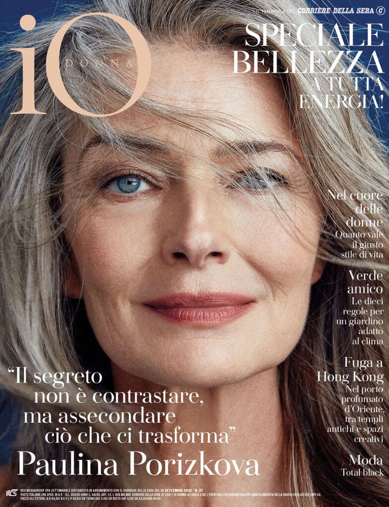 Close-up portrait of Paulina Porizkova on the cover of Io Donna magazine, showcasing her grey hair and blue eyes against a blue background.