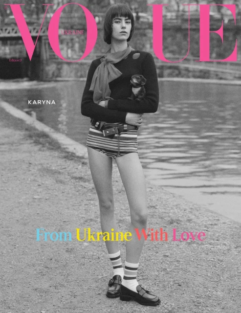 Vogue cover featuring a young woman in striped bottoms and a dark sweater, holding a small dog, with a river and architecture backdrop.