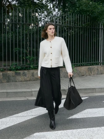Model wearing a white knit cardigan and black skirt walking on a street with a black handbag