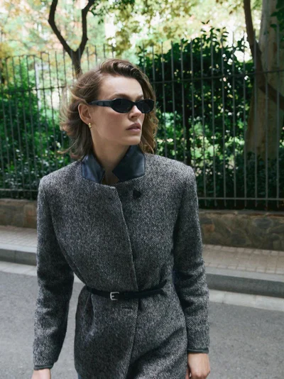 Model Cara Taylor in dark sunglasses and a grey tweed coat standing on a city street for Massimo Dutti