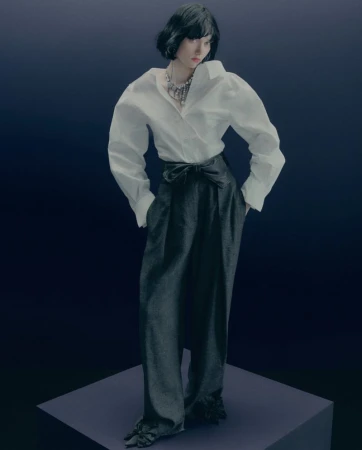 Woman posing in an oversized white shirt, wide-leg black trousers with tied waist, and a silver necklace on a gradient blue backdrop.