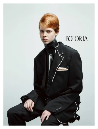Model with red hair wearing a black blazer and glossy neckpiece against a white background for Boloria #1 Collection