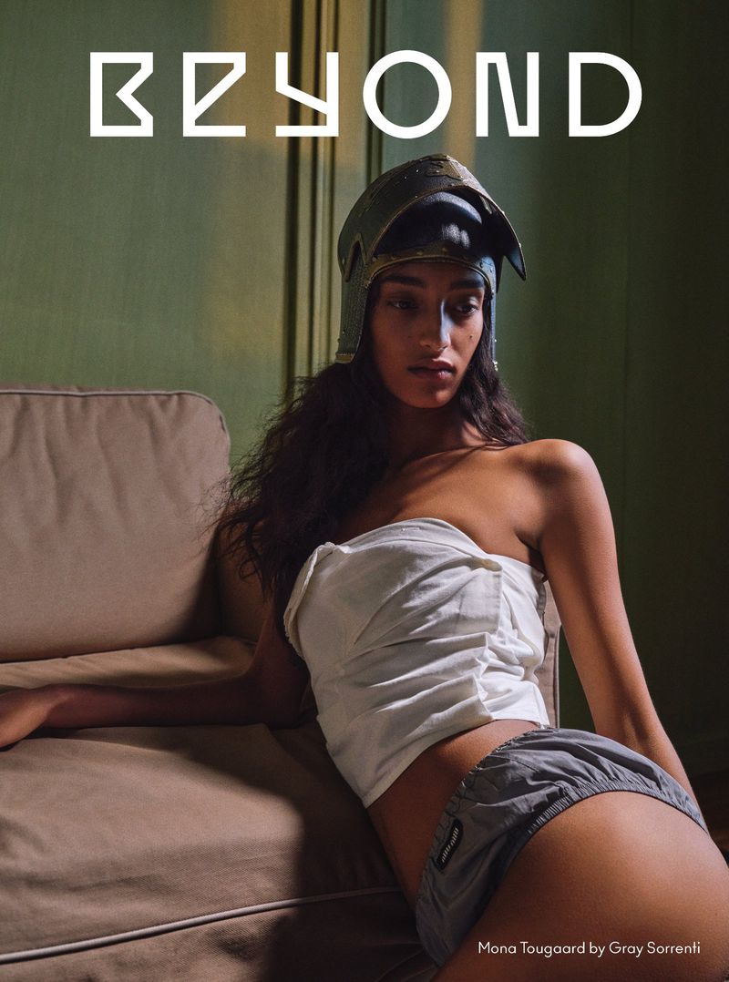 Portrait of a woman wearing a vintage-style helmet and a strapless top, reclining on a couch in an indoor setting with dim lighting.