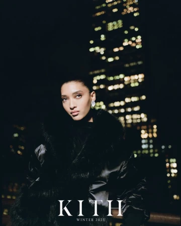 Model wearing a black winter coat against a dark skyscraper background with glowing windows at night