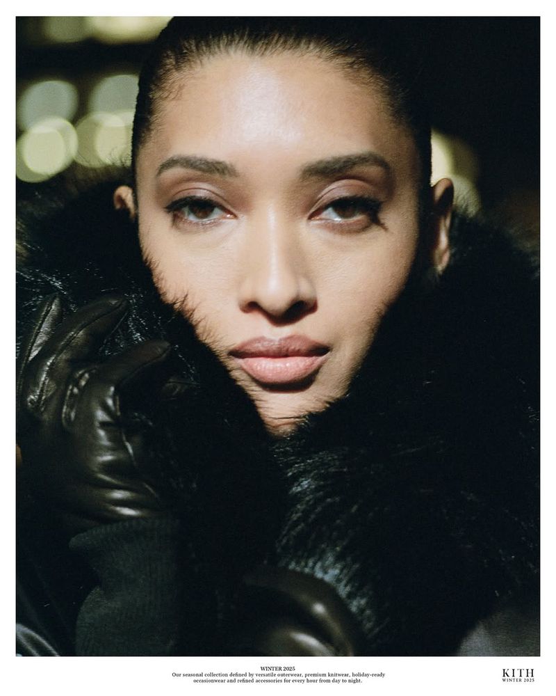 Close-up portrait of an adult woman wearing a dark fur collar and leather gloves against a blurred bokeh background, soft natural lighting.