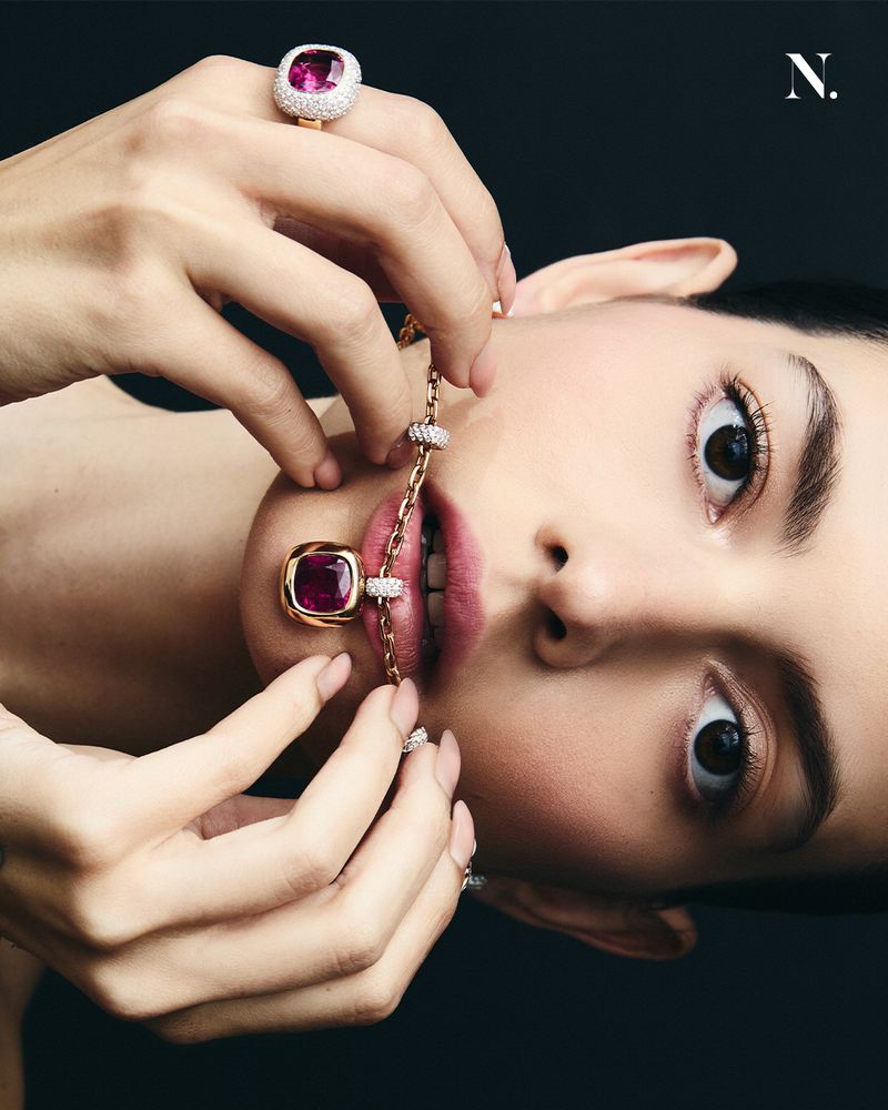 Portrait of a woman wearing gold jewelry including rings and a chain necklace against a dark background in a beauty shot.