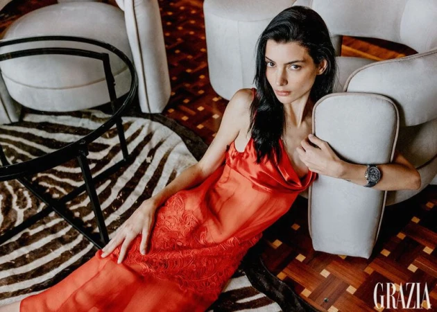 Brunette woman in a red dress lounging on the floor, flanked by cream armchairs and a zebra rug, in an indoor fashion editorial.