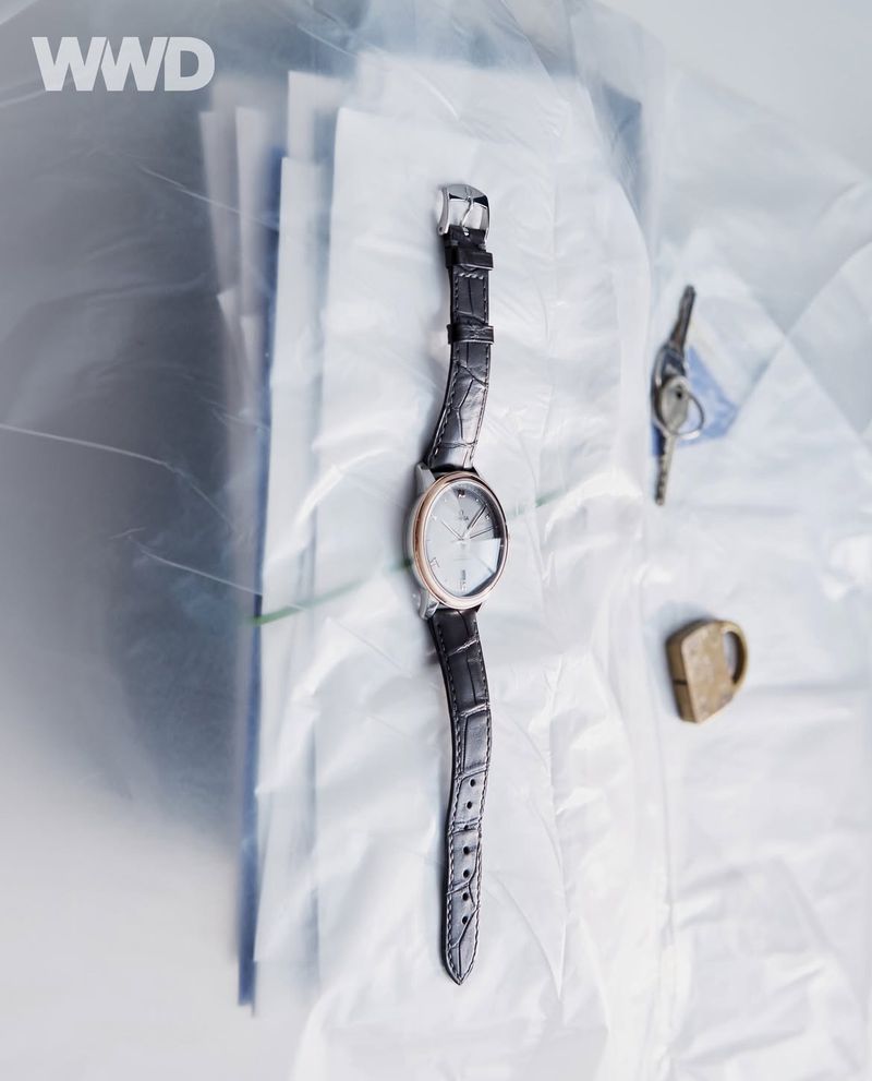 Elegant wristwatch with a leather strap lying on crinkled white fabric with keys and a padlock, set against a blurred background.