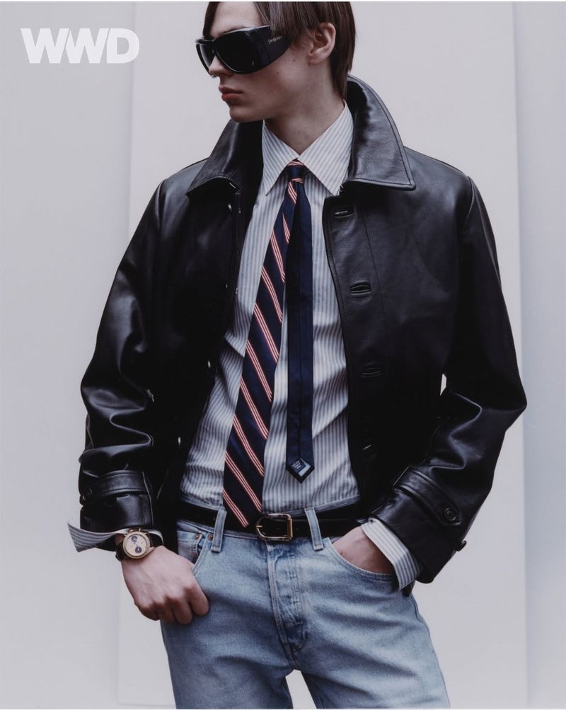A stylish male model wears sunglasses, a striped shirt, and a dark leather jacket in a studio shot for a fashion editorial.