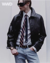 Model Max Vespa wearing a black leather jacket, striped tie, light blue jeans, and dark sunglasses against a plain studio background.