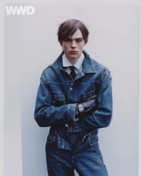 Male model wearing a denim jacket and matching jeans with arms crossed against a plain white background for WWD.