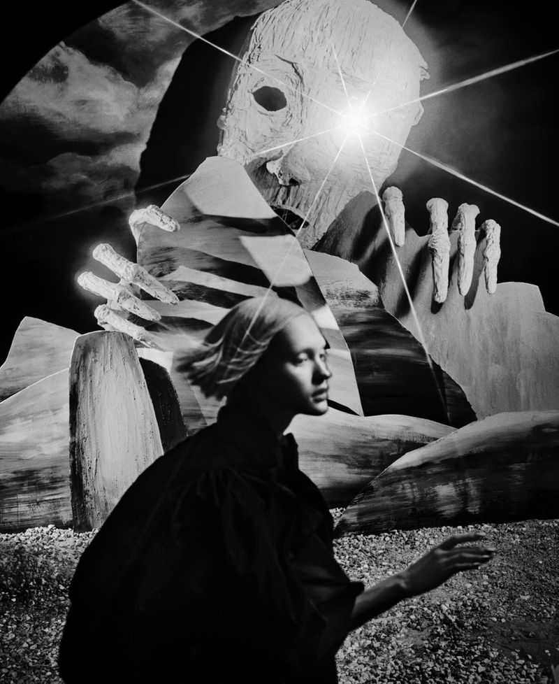 Monochrome image of a person in dark clothing with a head covering, standing before a looming, monstrous figure with an intense light.