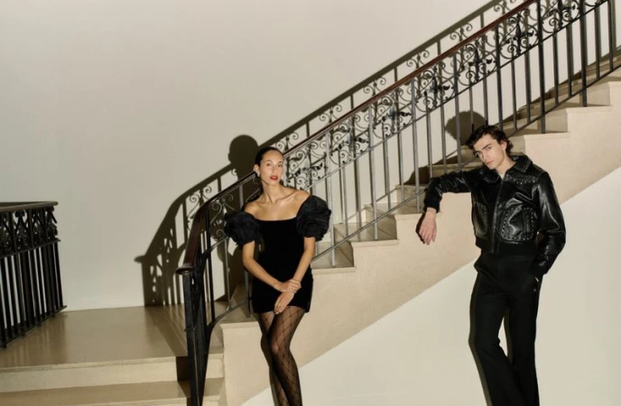 Elegant shot of a stylish woman in a black mini-dress and patterned tights, next to a man in leather jacket on a staircase.