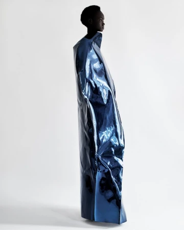 Fashion shot of a black model posing in a blue shiny vinyl-like dress in a bright photo studio, emphasizing shape and material.