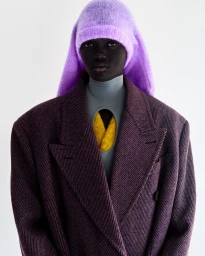 Model Achol Kuir wearing a purple knit hood and an oversized textured plum blazer against a white background.