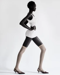 Model Achol Kuir wearing a white bodysuit and knee-high socks against a white studio seamless background
