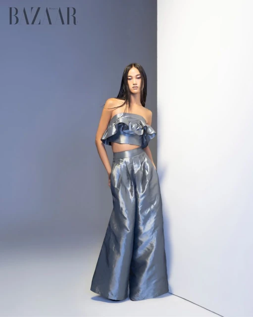 A slender female model poses in a studio wearing a metallic blue two-piece ruffled crop top and palazzo pants for a fashion editorial.