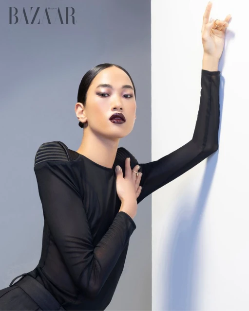 A sleek portrait features a model in a black outfit against a grey and white backdrop, accented with minimalist makeup and jewelry.