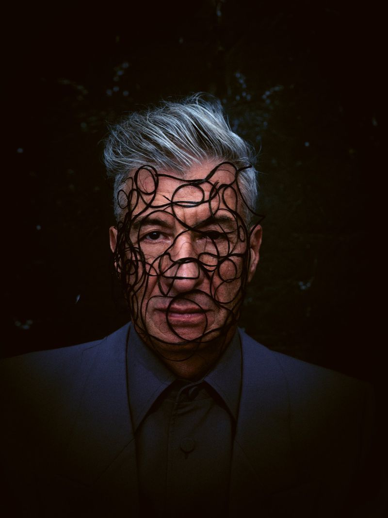 Striking close-up portrait of a mature adult man with silver hair, wearing a blue suit and a mask made of intertwined black cords.