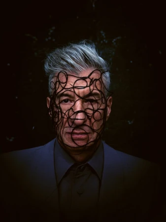 Striking close-up portrait of a mature adult man with silver hair, wearing a blue suit and a mask made of intertwined black cords.