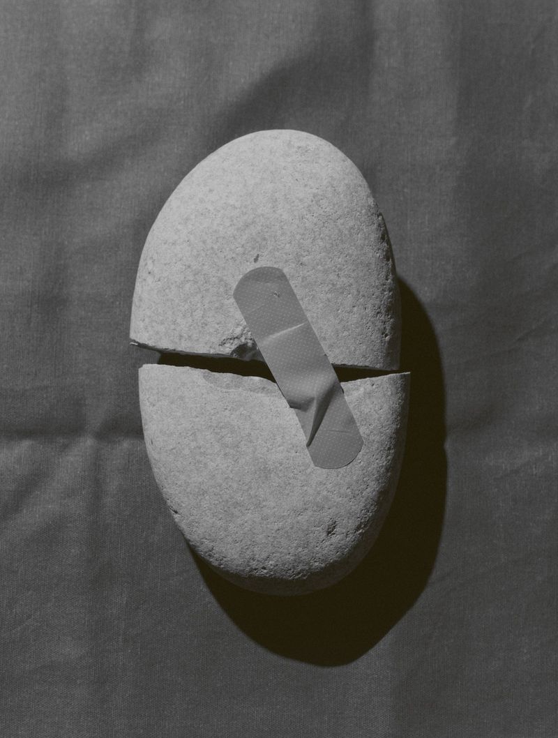 Monochrome studio shot of a grey stone broken in half, joined by a bandage, creating a symbolic image with textural background.
