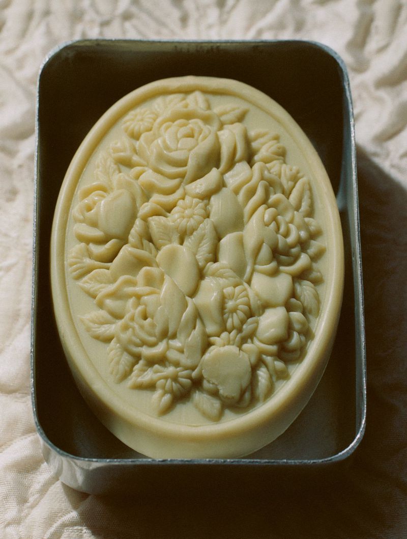 Artisan soap bar with floral design in a metal tin on a textured cloth surface, showcasing craftsmanship and delicate patterns.