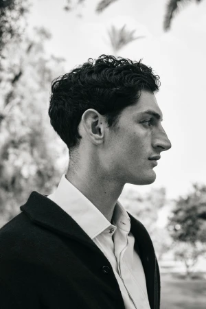Profile portrait of a male model in a white shirt and dark jacket outdoors with trees