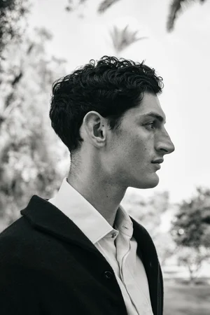 Profile portrait of a male model in a white shirt and dark jacket outdoors with trees