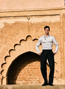 Model Aaron Shandel posing against an arched brick wall for GQ Espana editorial Al sol de invierno