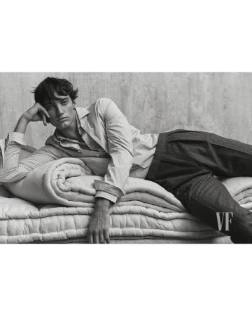 Model Théo le Grelle reclines on quilted mattresses wearing a striped button-down shirt and dark pleated trousers in black and white.
