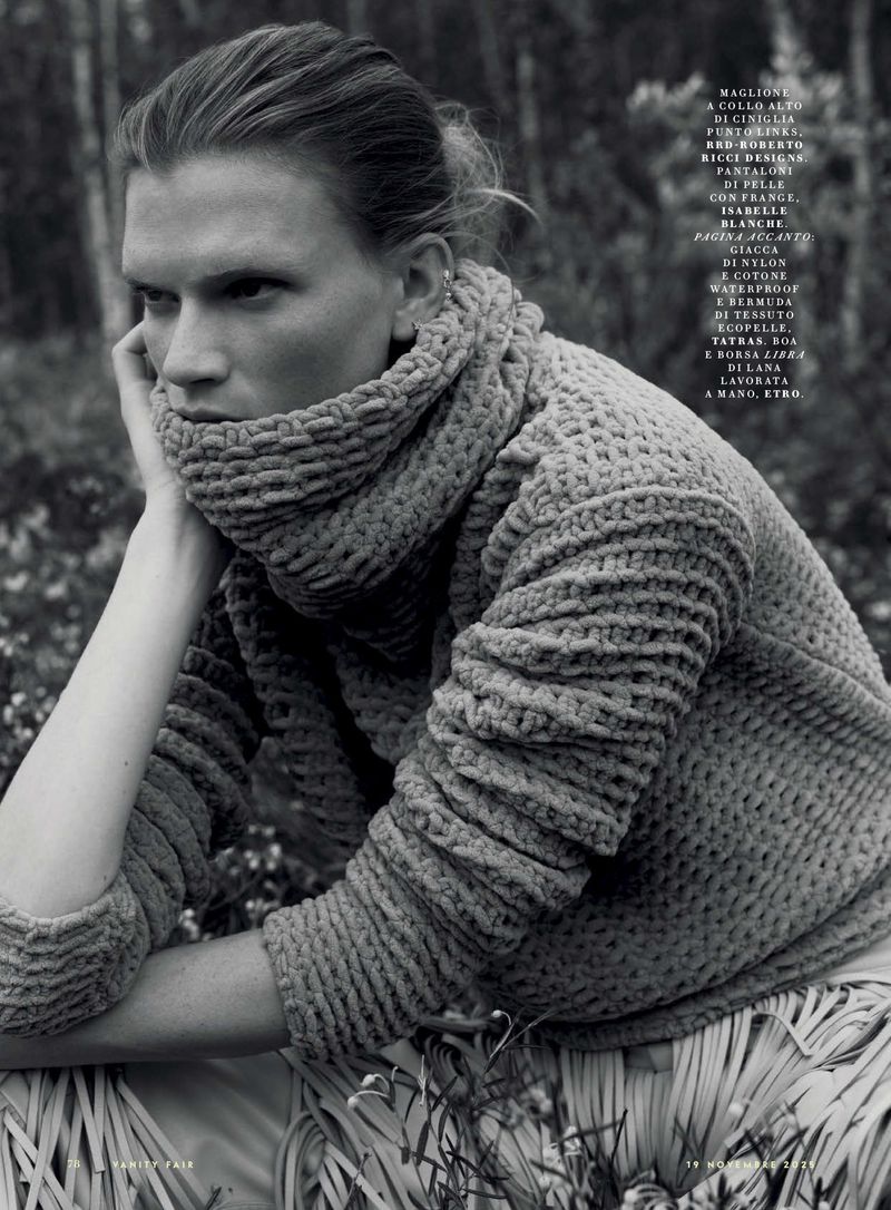 Monochrome portrait of a posed adult female wearing a textured, high-neck sweater in an outdoor setting with a forest background.