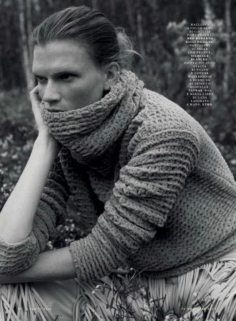 Monochrome portrait of a posed adult female wearing a textured, high-neck sweater in an outdoor setting with a forest background.