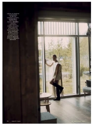 Model standing by a large window in a light dress and black boots, viewed through a doorway for Vanity Fair Italia