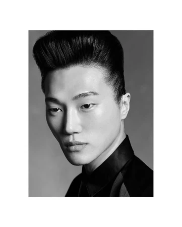 Striking black and white portrait of an Asian man with a pompadour hairstyle, wearing a dark collared shirt, against a gray background.