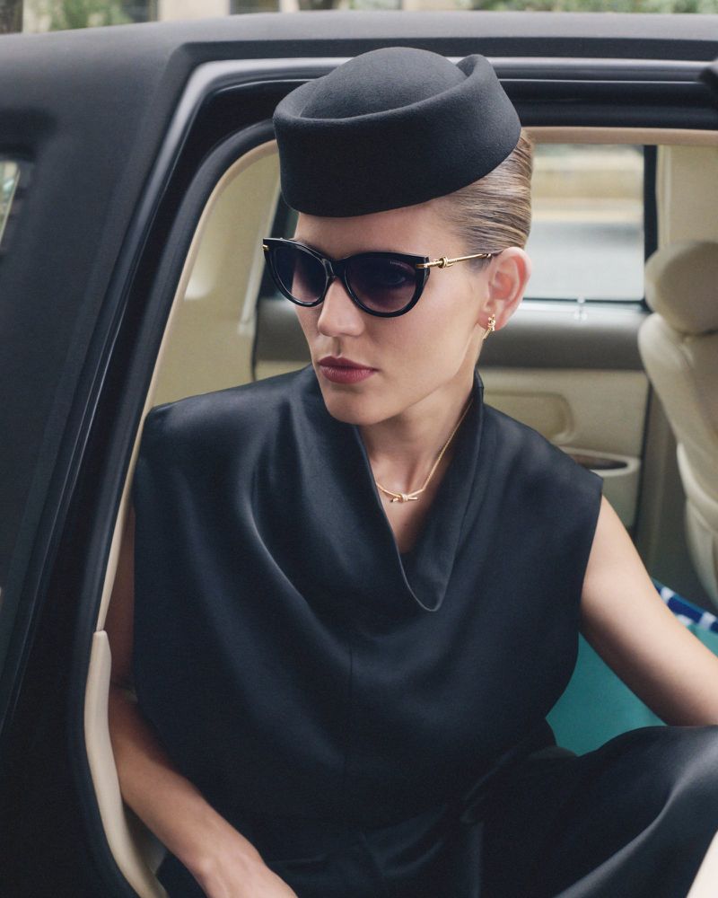 Elegant woman in sunglasses and black hat seated in a car. Classic, poised, and stylish for fashion or beauty advertising.